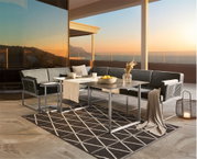 Moderner Loungetisch auf einer Terrasse mit Blick auf den Sonnenuntergang, umgeben von stilvollen Sofas und dekorativen Elementen, aus seitlicher Perspektive.