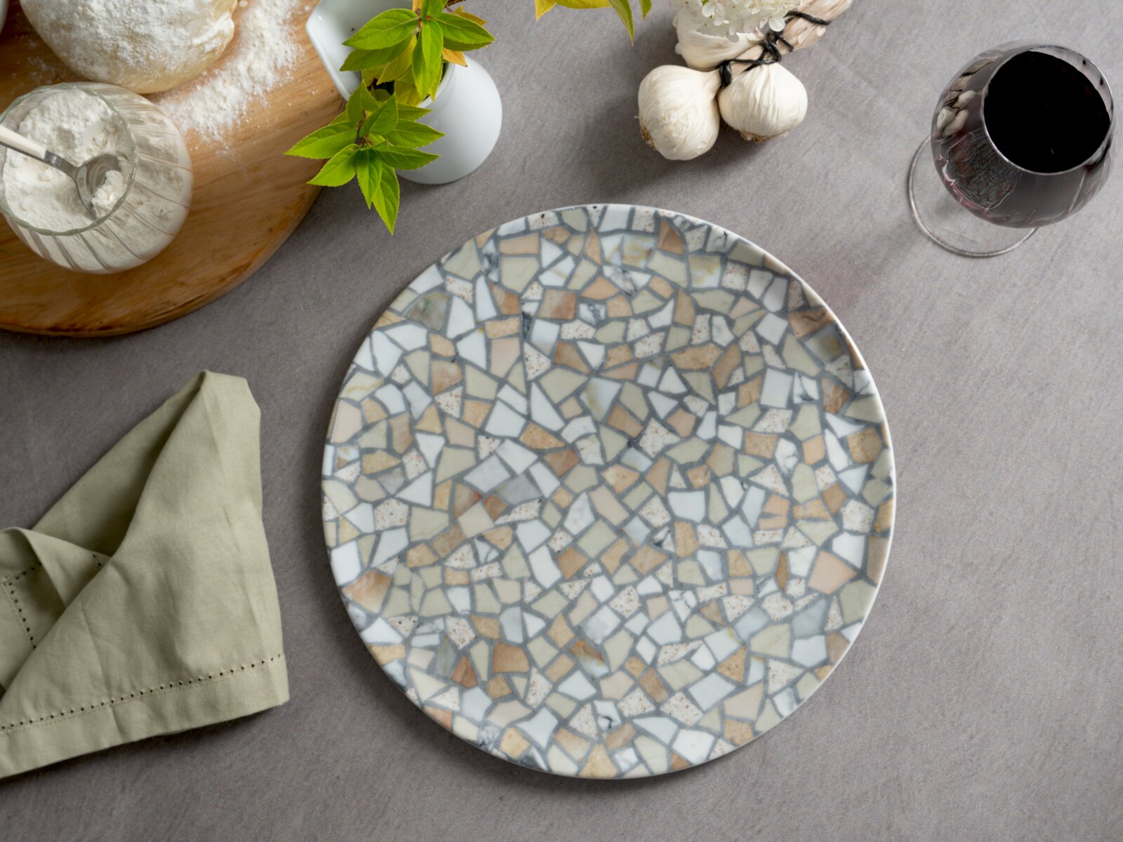Runder Keramikteller mit Terrazzo-Muster in Beige, Grau und Weiß auf gedecktem Tisch, Draufsicht von oben.