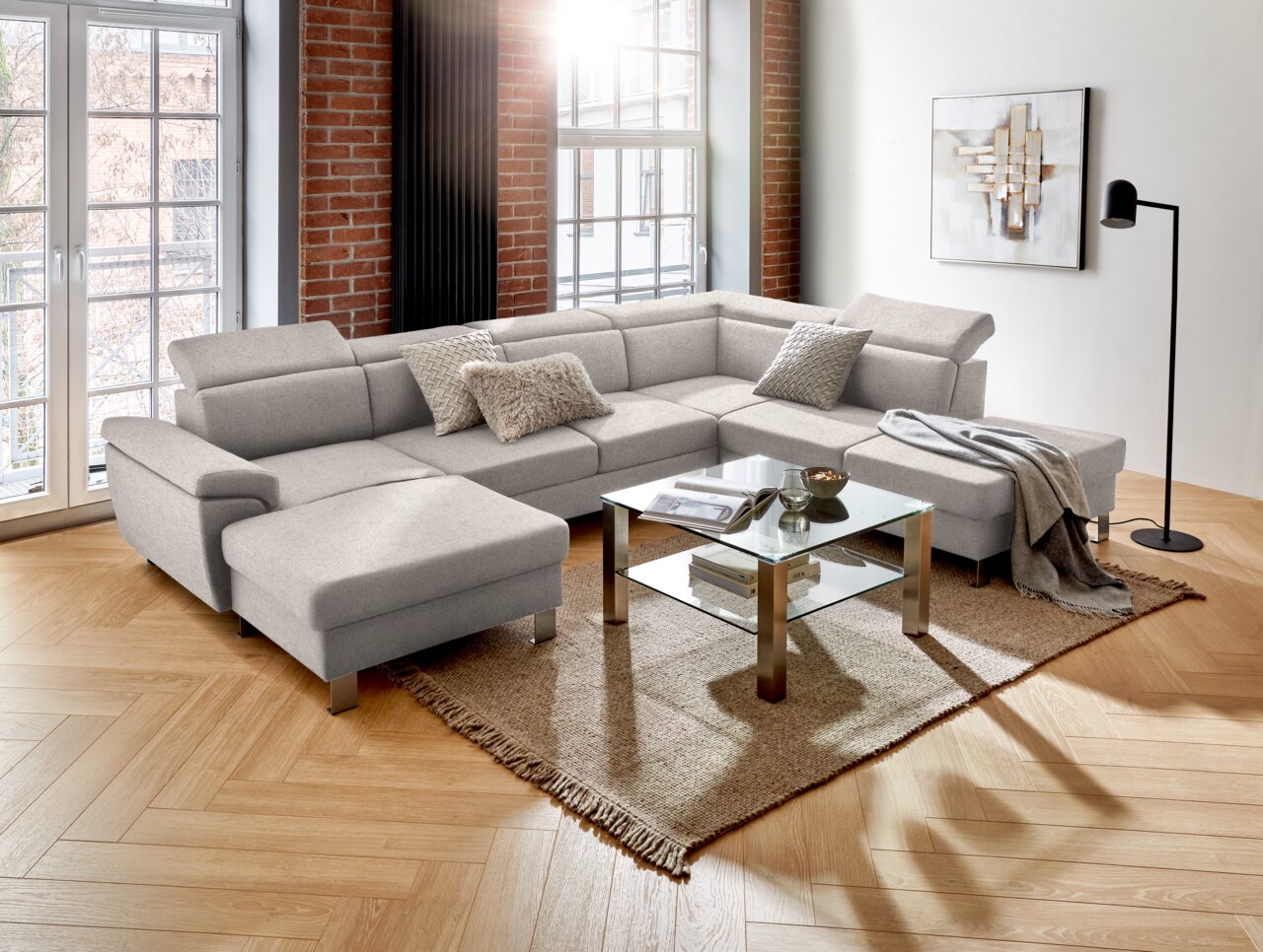 Moderne graue Rundecke in U-Form in einem stilvollen Wohnzimmer mit Holzboden, großen Fenstern und dekorativen Kissen, aus der Perspektive von vorne links betrachtet.