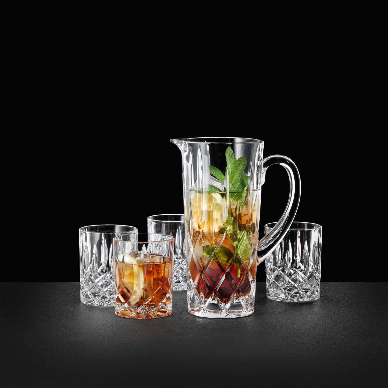 Krugset 5-tlg. Noblesse aus Kristallglas, bestehend aus einem Krug und vier Gläsern, auf schwarzem Hintergrund. Der Krug ist mit Getränk und Minzblättern gefüllt, seitliche Perspektive.