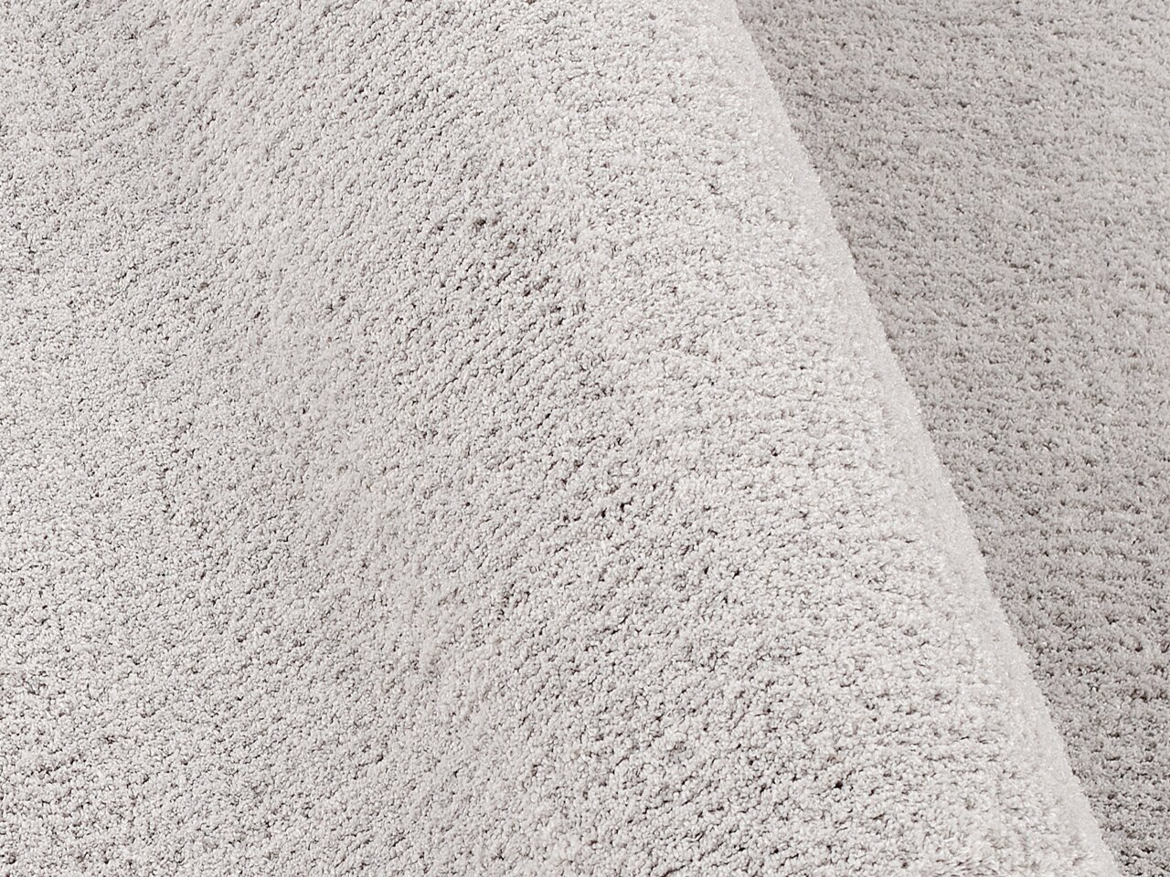 Nahaufnahme einer weichen, hellgrauen Textur eines Teppichs in der Größe von ca. 200x250cm, perspektivisch von der Seite aufgenommen.