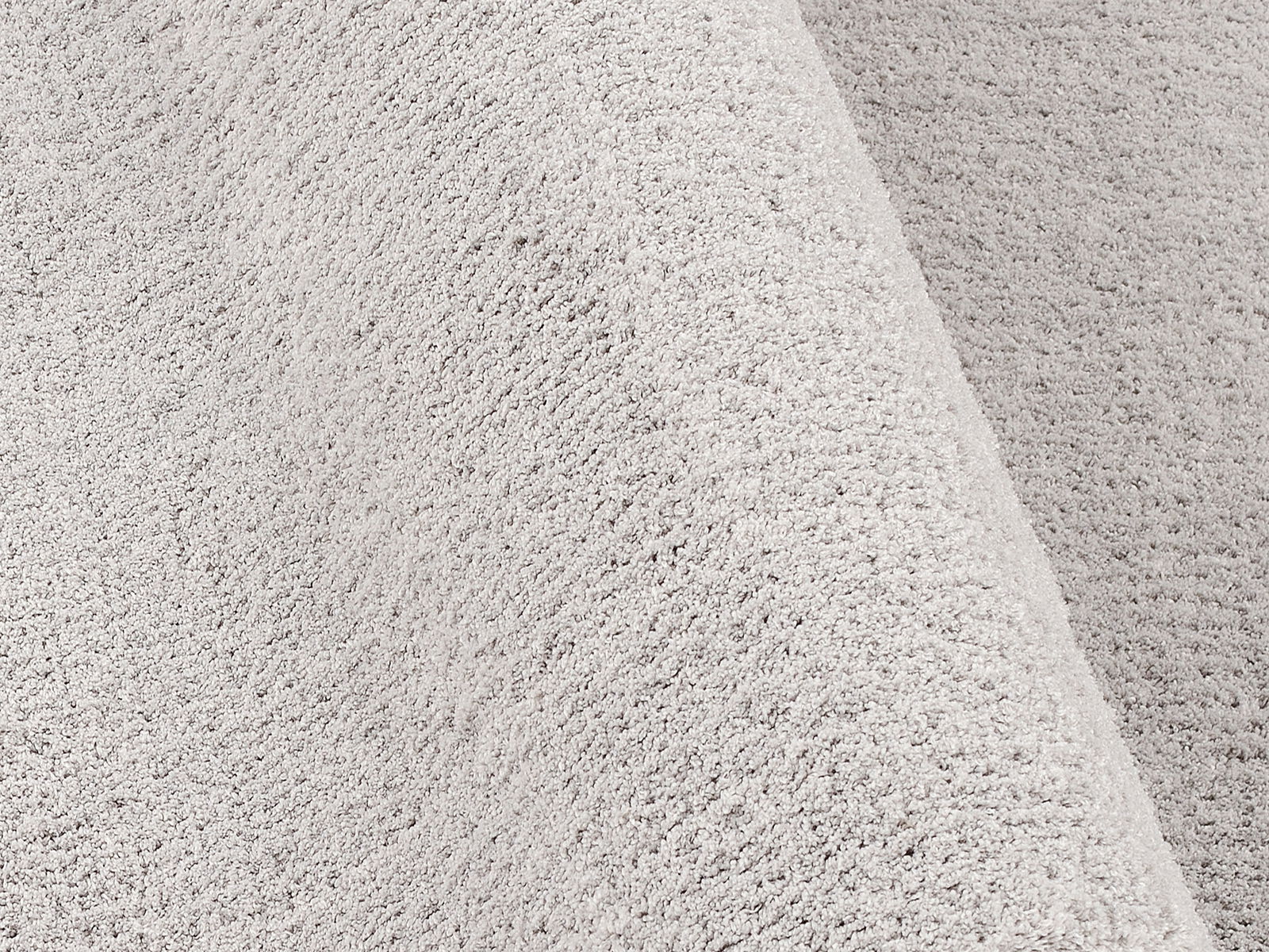 Nahaufnahme einer weichen, hellgrauen Textur eines Teppichs in der Größe von ca. 200x250cm, perspektivisch von der Seite aufgenommen.