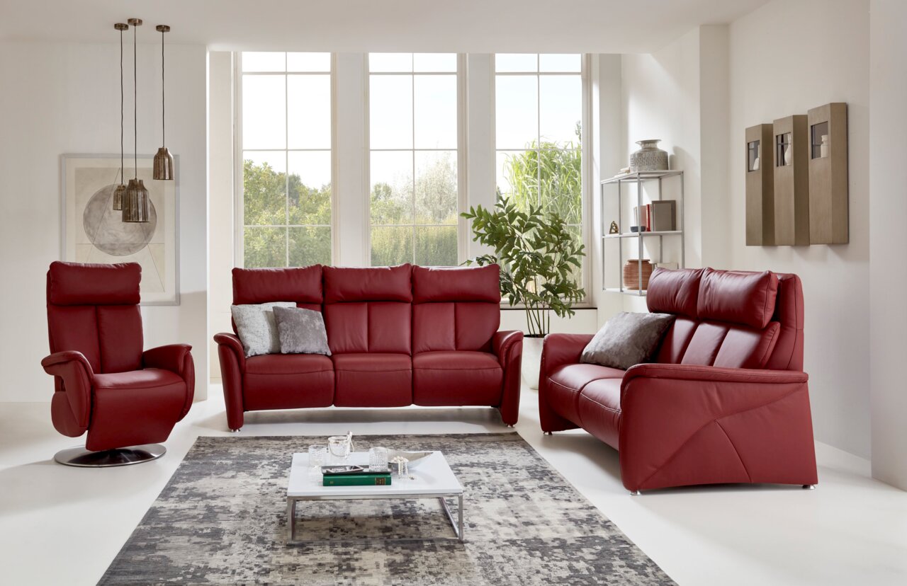 Rotes Ledersofa-Set bestehend aus einem Dreisitzer, einem Zweisitzer und einem Sessel in einem modernen Wohnzimmer mit großen Fenstern und stilvoller Dekoration, Frontalansicht.