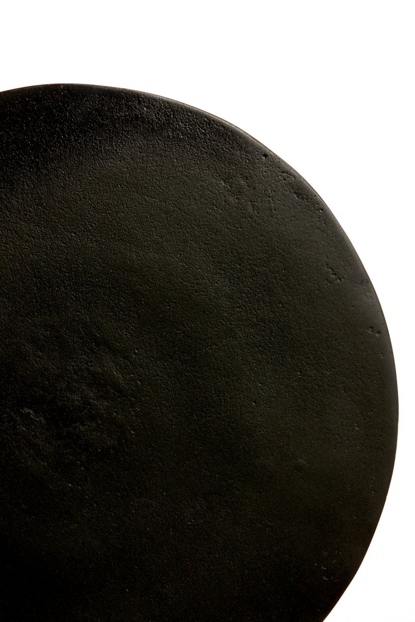 Nahaufnahme der Tischplatte eines runden Beistelltisches in schwarzer Farbe, von oben betrachtet.