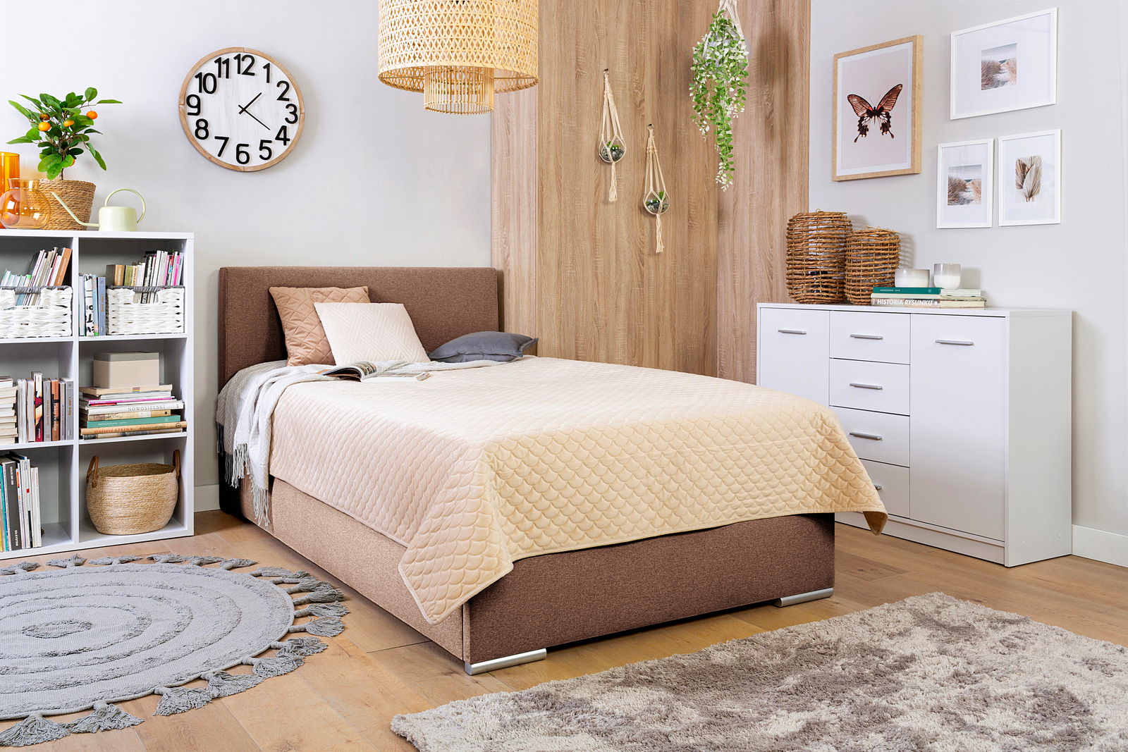 Gemütliches Schlafzimmer mit Boxbett 140 in braunem Stoff, dekoriert mit Kissen und Decke, umgeben von modernen Möbeln und Pflanzen, seitliche Perspektive.