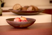 Donkerbruine houten fruitschaal met granaatappels, schuin van voren gezien in een warm interieur