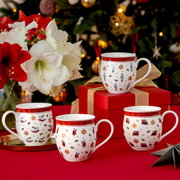 Vier festliche Jubiläums-Becher mit weihnachtlichen Motiven, präsentiert auf einem Tisch mit rotem Tischtuch, im Hintergrund ein geschmückter Weihnachtsbaum. Perspektive: Frontalansicht.
