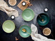 Drei glasierte Keramikschalen in Mint- und Petrolgrün mit goldfarbenen Löffeln, dekoriert mit Leinentuch, Teelichtern und Naturdetails auf dunkler Oberfläche, fotografiert in Draufsicht (Flatlay)