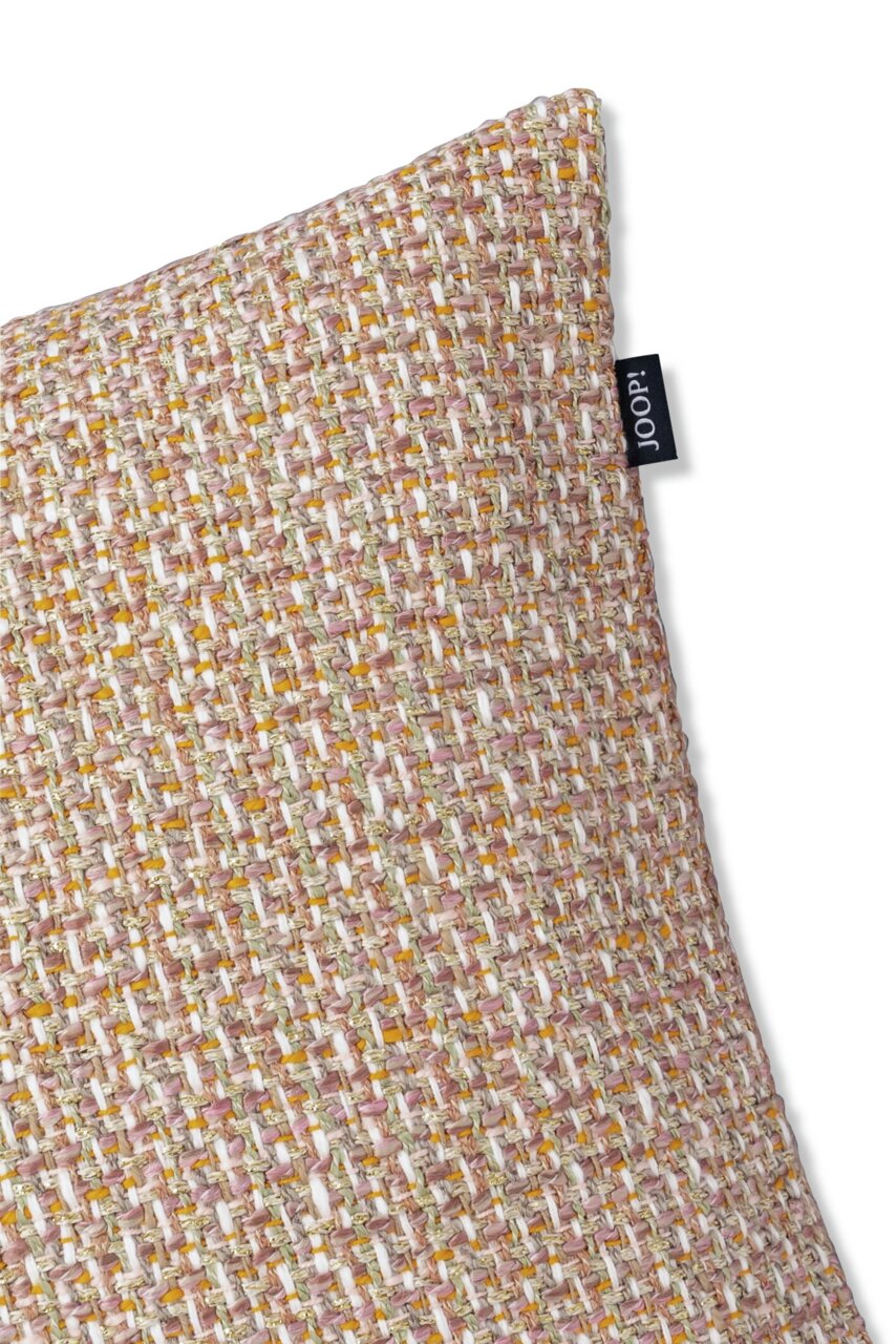 Nahaufnahme einer strukturierten Zierkissenhülle in beige und braun mit einem kleinen schwarzen Etikett an der Seite, perspektivisch von oben fotografiert.