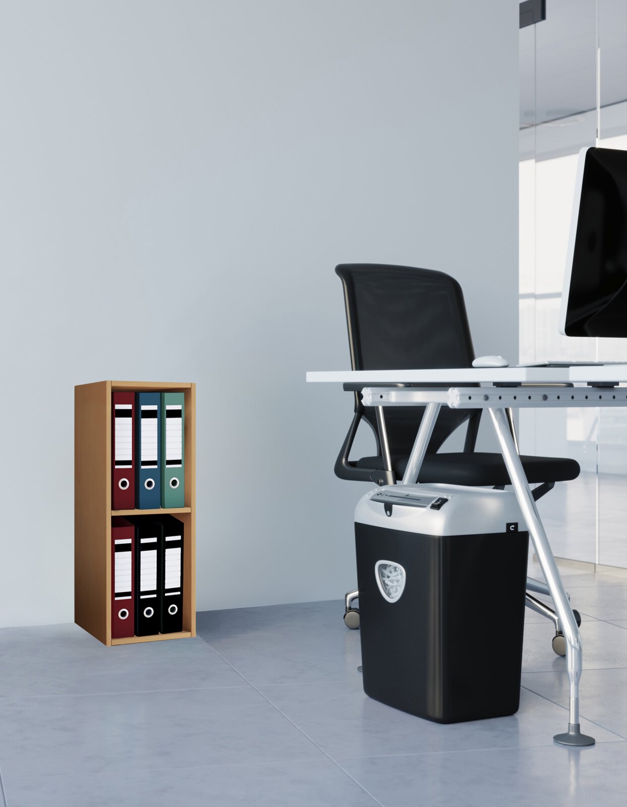 Schwarzer Aktenvernichter unter einem modernen Büroschreibtisch, rechts im Bild aus leicht seitlicher Perspektive, mit Ordnerregal im Hintergrund