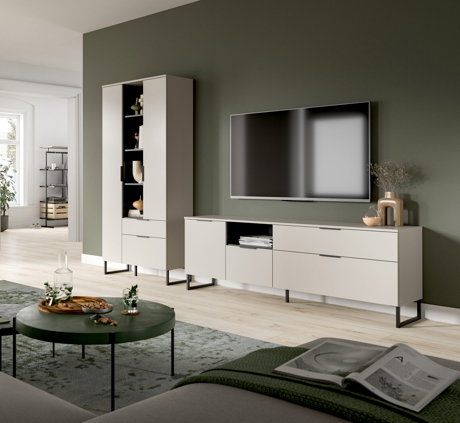 Modernes Wohnzimmer-Setup mit hellbeigem TV-Lowboard und passendem Hochschrank auf schwarzen Metallfüßen, wandmontiertem Fernseher und Deko vor olivgrüner Wand, perspektivisch in leichter Schrägansicht von vorn.