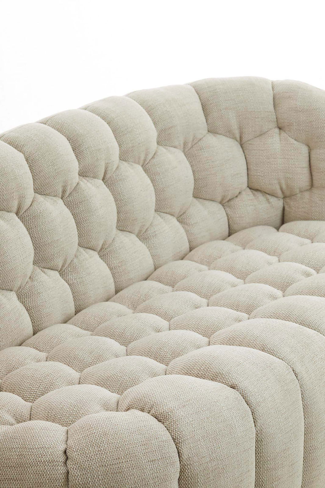 Detailansicht einer beigen Couch mit gepolstertem, gestepptem Stoffbezug aus der Seitenperspektive.