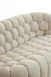 Detailansicht einer beigen Couch mit gepolstertem, gestepptem Stoffbezug aus der Seitenperspektive.