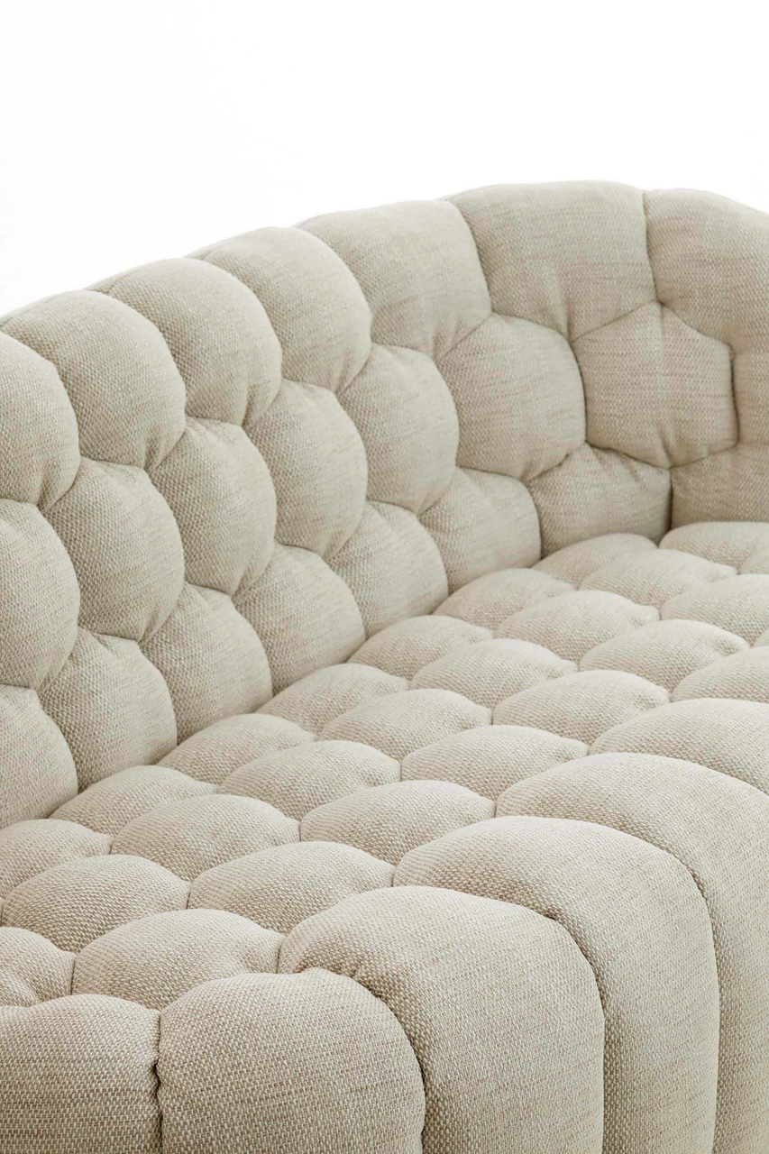 Detailansicht einer beigen Couch mit gepolstertem, gestepptem Stoffbezug aus der Seitenperspektive.