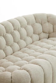 Detailansicht einer beigen Couch mit gepolstertem, gestepptem Stoffbezug aus der Seitenperspektive.