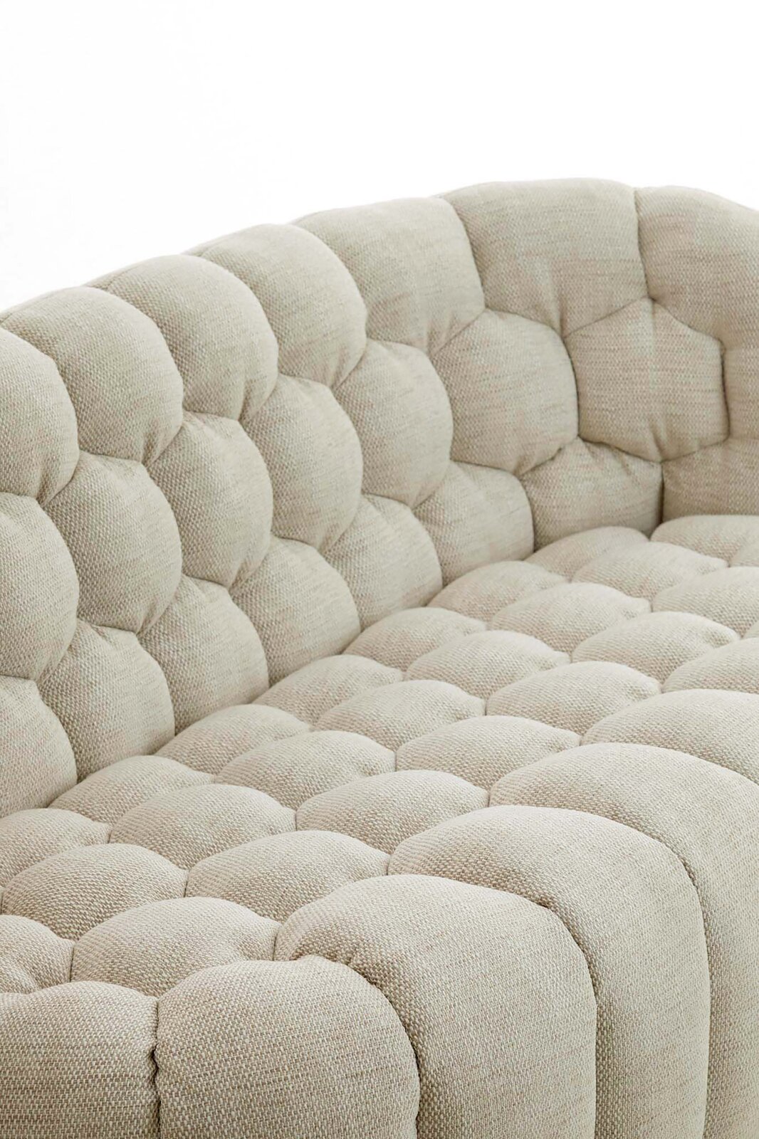 Detailansicht einer beigen Couch mit gepolstertem, gestepptem Stoffbezug aus der Seitenperspektive.