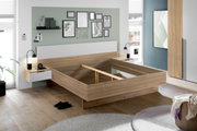 Moderne slaapkamer met een stijlvol houten bedframe, geflankeerd door twee nachtkastjes met lampjes, in een lichte en uitnodigende omgeving. Aanzicht van linksvoor.