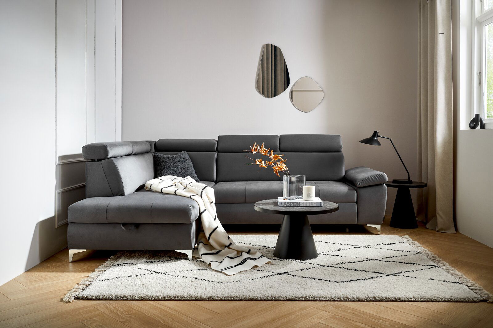 Graue Rundecke Osca in modernem Wohnzimmer, seitliche Perspektive, mit Kissen und Decke dekoriert, auf hellem Teppich.