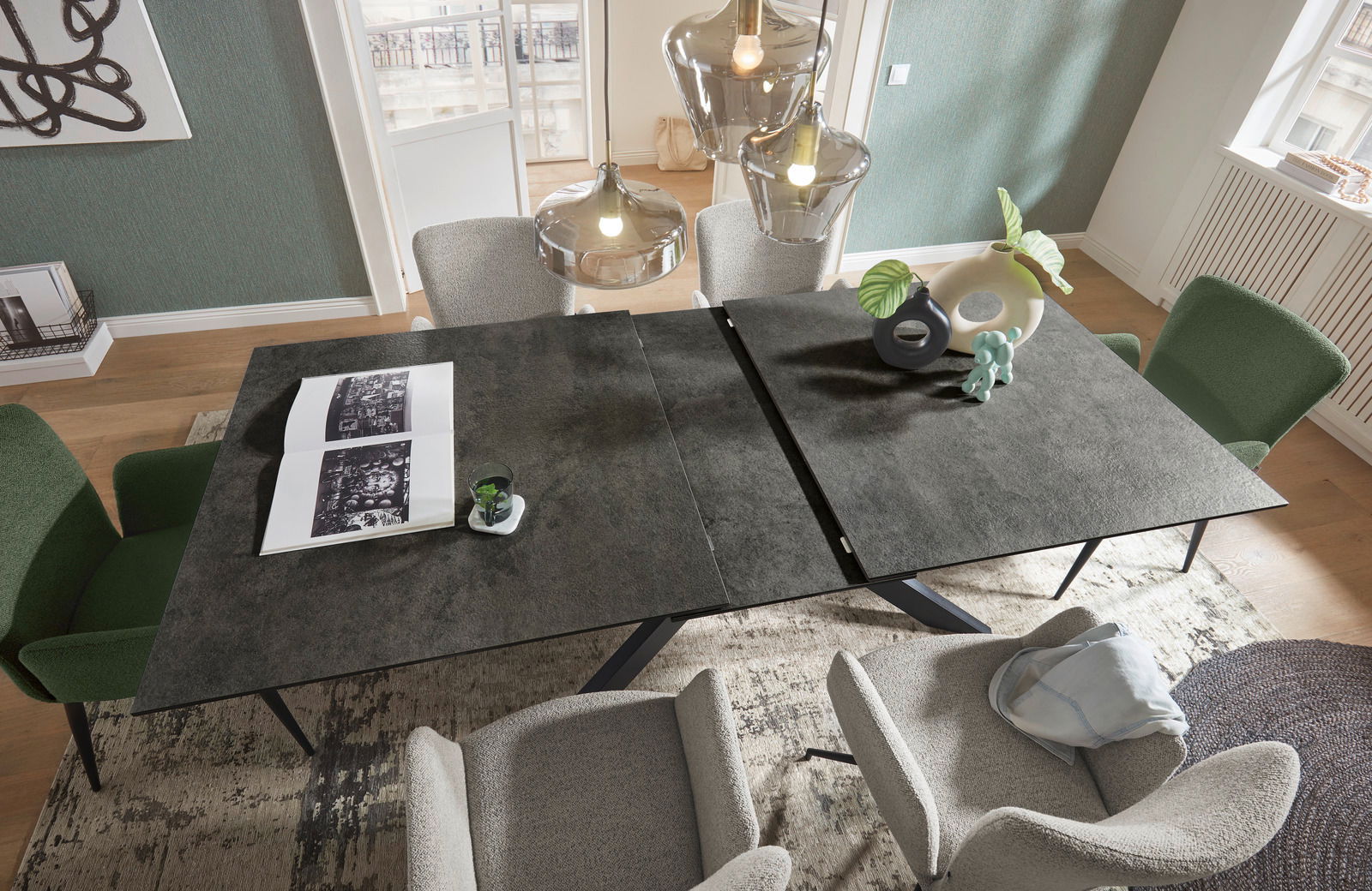 Moderner Esstisch mit dunkler Tischplatte, umgeben von grünen und grauen Stühlen, aus der Vogelperspektive fotografiert.