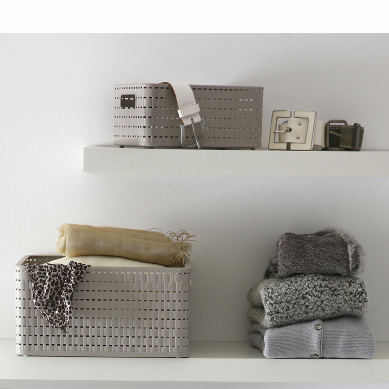Zwei beige Aufbewahrungskörbe im COUNTRY-Stil auf weißen Regalen, einer mit einem Gürtel und Accessoires, der andere mit einem Tuch und Kleidung, seitliche Perspektive.