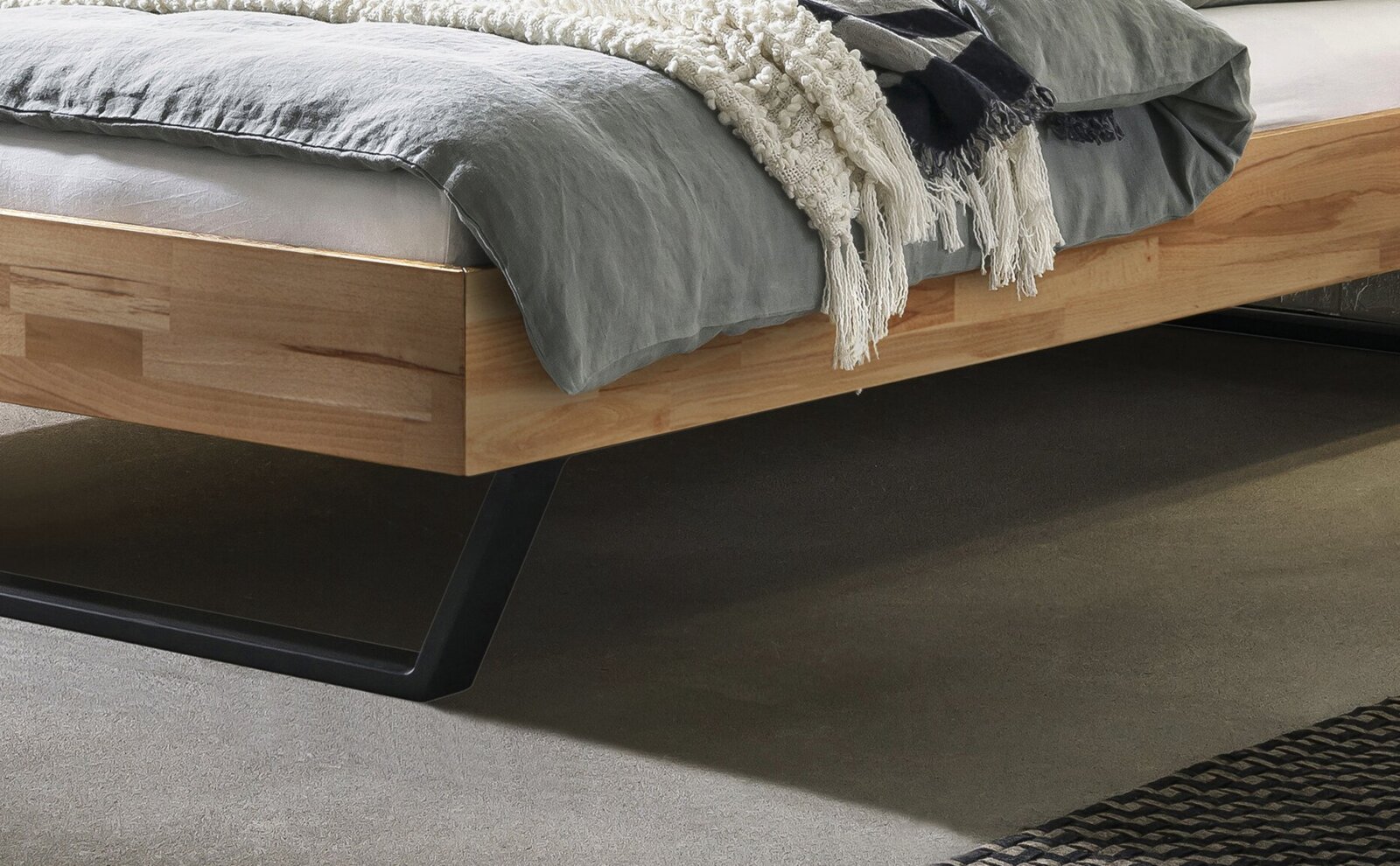 Modernes Holzbett mit schwarzem Kufengestell aus Metall und grauer Bettwäsche, Detailansicht aus seitlicher Perspektive auf Rahmen und Unterbau