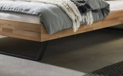 Modernes Holzbett mit schwarzem Kufengestell aus Metall und grauer Bettwäsche, Detailansicht aus seitlicher Perspektive auf Rahmen und Unterbau
