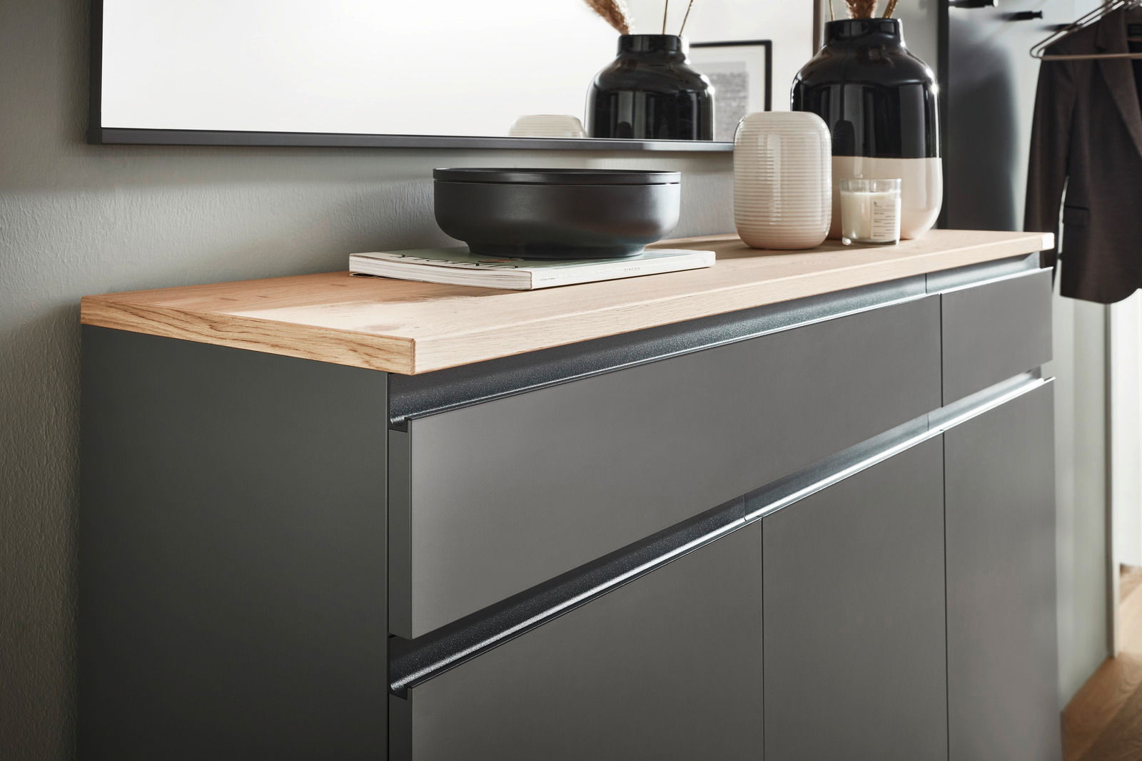 Nahaufnahme eines modernen Garderoben-Sets mit dunklen Schubladen und heller Holzoberfläche, dekoriert mit Vasen und einer Schale.