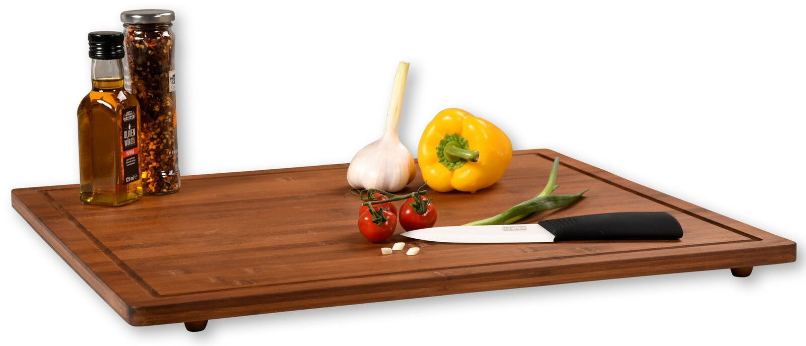 Holz-Schneidebrett mit erhöhten Kanten, darauf liegen eine gelbe Paprika, Knoblauch, Tomaten, Frühlingszwiebel, ein Messer und Gewürzflaschen. Perspektive: seitlich.