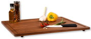 Houten snijplank met opstaande randen, met daarop een gele paprika, knoflook, tomaten, een lente-ui, een mes en kruidenpotjes. Perspectief: zijaanzicht.