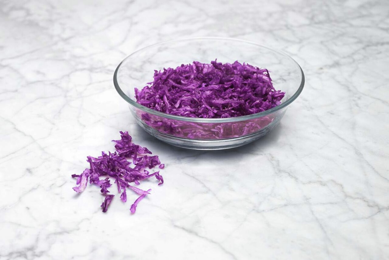 Eine Glasschüssel mit frisch geriebenem Rotkohl auf einer Marmoroberfläche, fotografiert aus der Vogelperspektive.