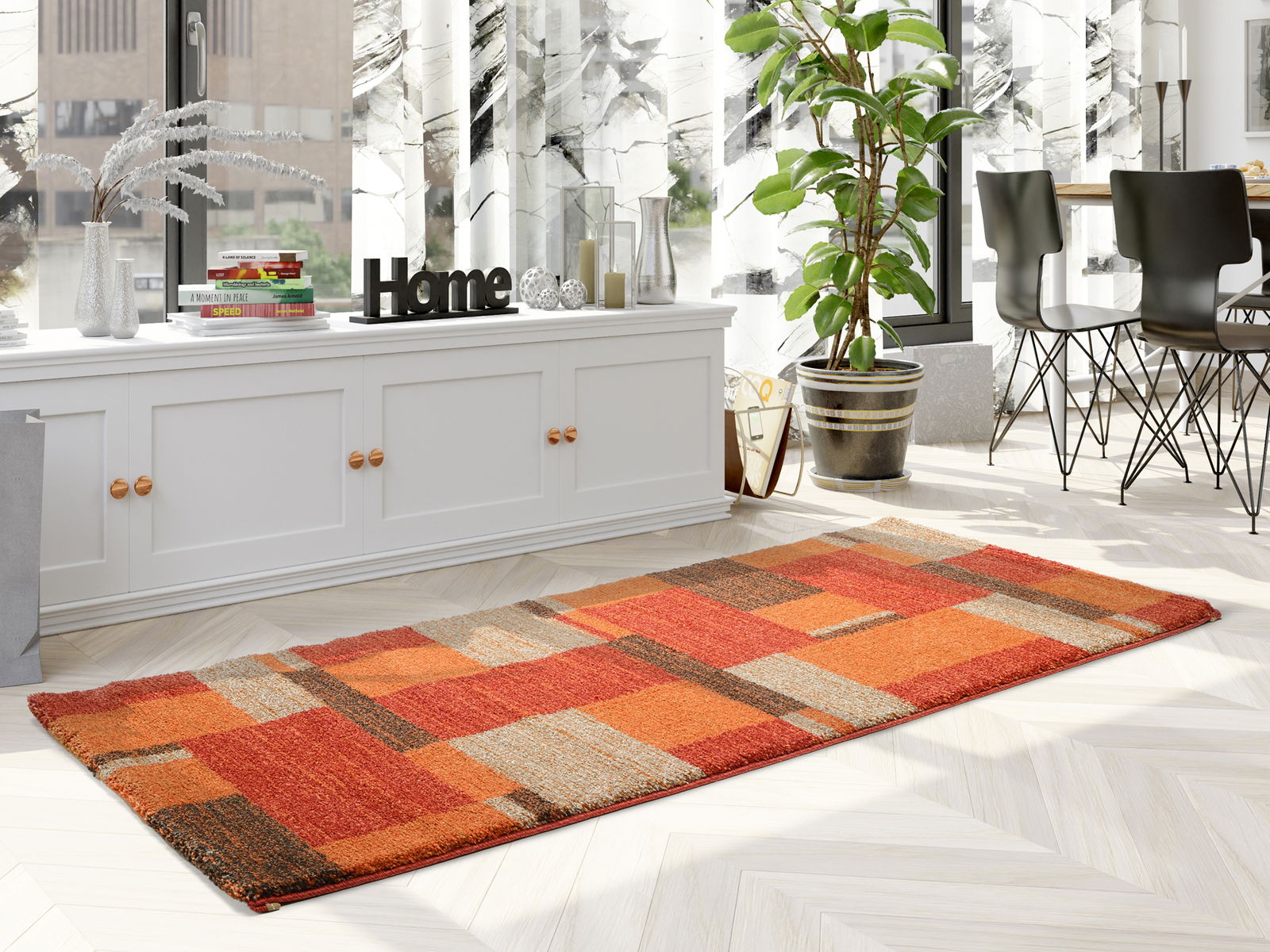 Moderner Teppich in warmen Rottönen mit geometrischem Muster, auf einem hellen Holzboden in einem stilvoll eingerichteten Raum mit Pflanzen und Dekorationen, aus seitlicher Perspektive fotografiert.