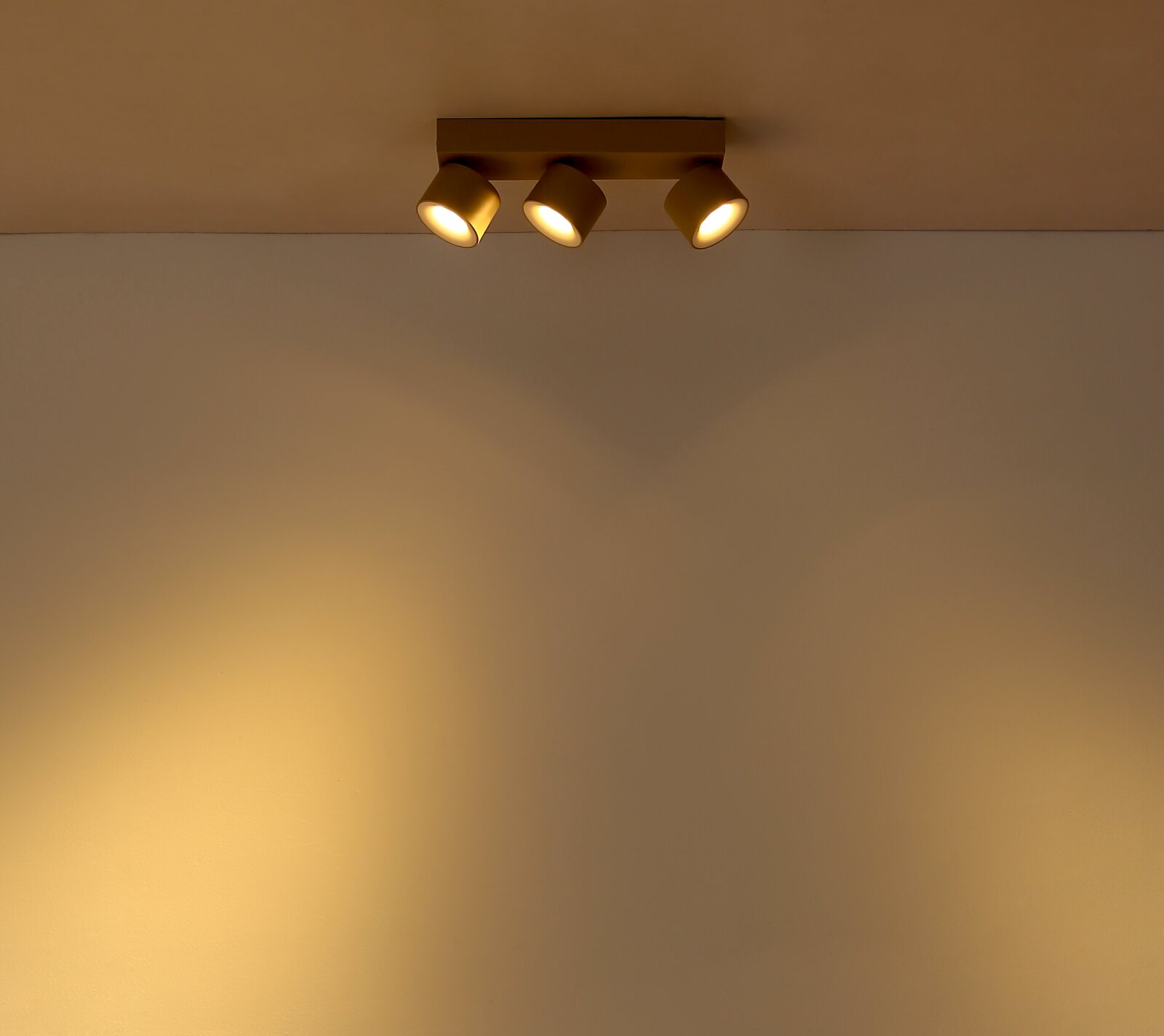 Dreiflammiger Deckenstrahler in Gold/Champagner mit warmweißem Licht an weißer Decke, leicht von unten aufgenommen (Untersicht).
