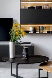 Moderner Couchtisch mit dunkler runder Tischplatte und schlanken Metallbeinen, dekoriert mit einer hohen Vase mit gelben Blumen, aus der Perspektive von vorne.