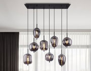 Moderne hanglamp BLACKY met meerdere rookgrijze glazen bollen, van onderaf gezien, voor een raam met gordijnen.