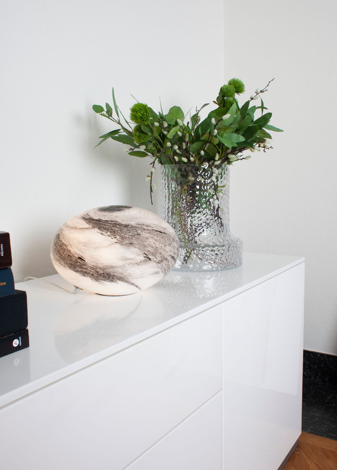 Moderne Tischleuchte in Marmoroptik auf einem weißen Schrank, seitliche Perspektive