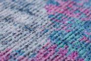 Nahaufnahme eines bunten Teppichs mit einem Muster in Blau-, Rosa- und Grautönen, aus seitlicher Perspektive.