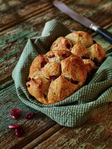 Nahaufnahme von frisch gebackenen Brötchen mit Cranberries auf einem rustikalen Holztisch, präsentiert in einem grünen Tuch.