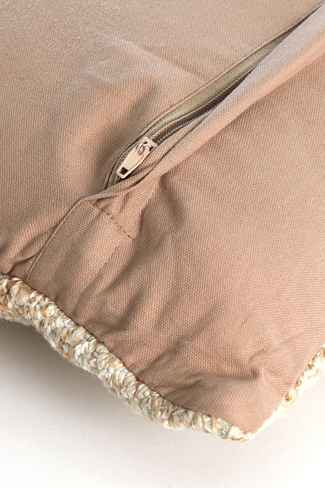 Nahaufnahme eines beigen Kissens mit Reißverschluss und geflochtener Kante.