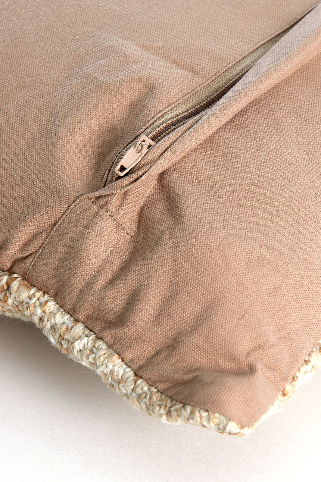 Nahaufnahme eines beigen Kissens mit Reißverschluss und geflochtener Kante.