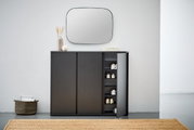 Moderner schwarzer Schuhschrank mit geöffneter Tür, der von vorne gezeigt wird. Im Inneren sind mehrere Paar Schuhe sichtbar. Der Schrank steht in einem minimalistischen Raum mit einem Spiegel darüber und Dekorationen darauf.