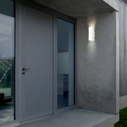 Moderne Akku-Außenwandleuchte an einer Betonwand neben einer Haustür, seitliche Perspektive