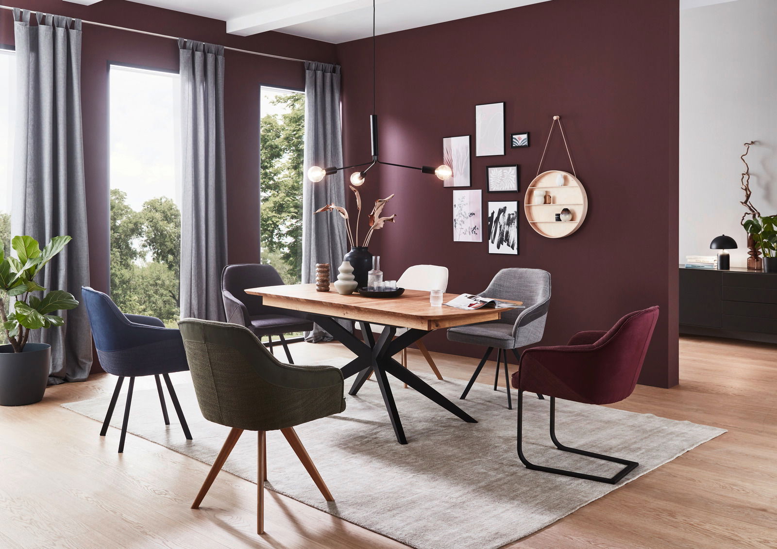 Esszimmer mit modernem Esstisch aus Holz und verschiedenen Stühlen in einem stilvoll eingerichteten Raum mit großen Fenstern und dekorativer Wandgestaltung. Perspektive: seitlich.