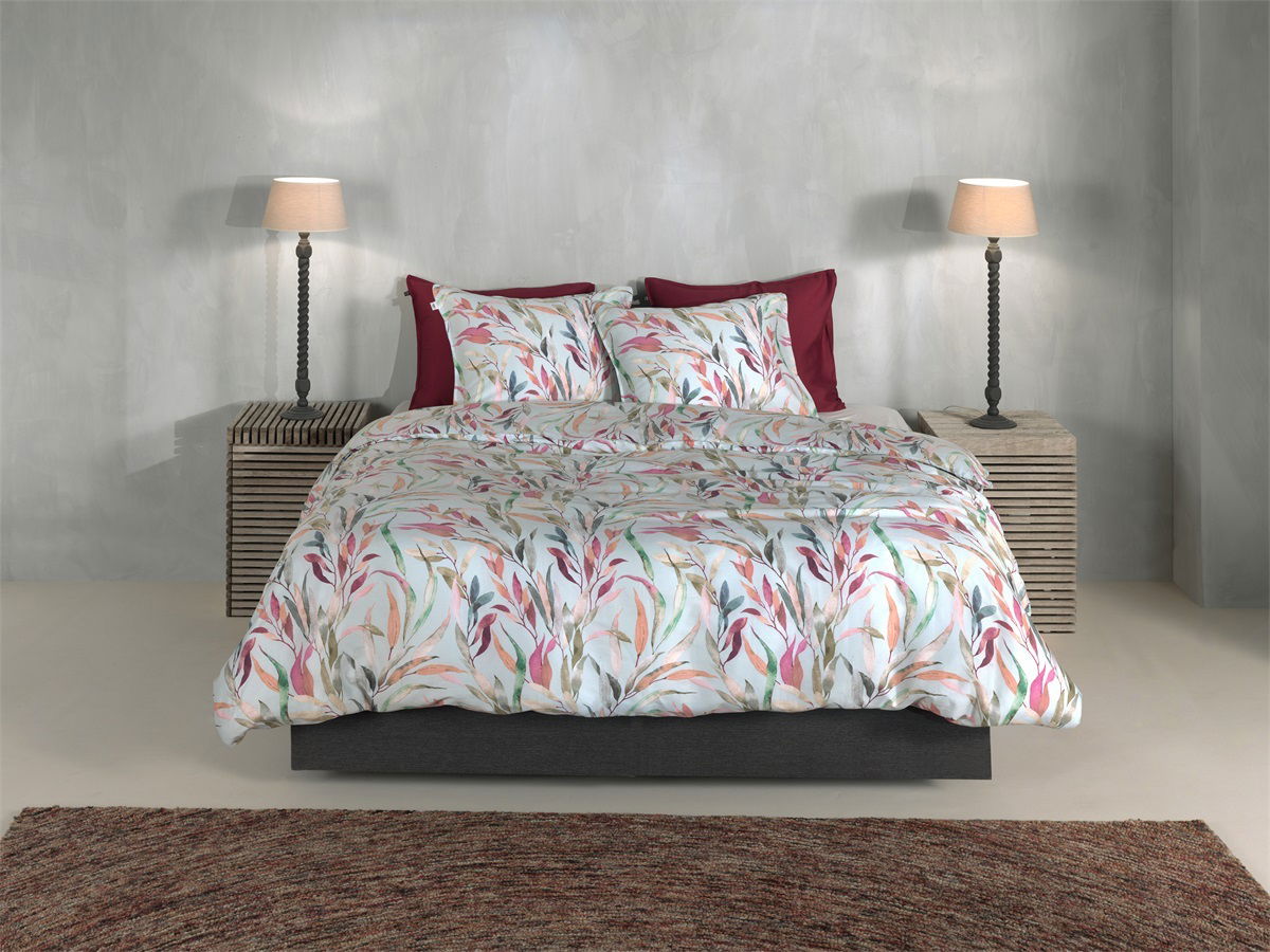 Bett mit floraler Bettwäsche in sanften Farben, frontal fotografiert, mit zwei Nachttischen und Lampen.