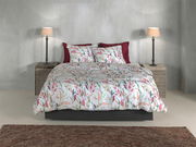 Bett mit floraler Bettwäsche in sanften Farben, frontal fotografiert, mit zwei Nachttischen und Lampen.