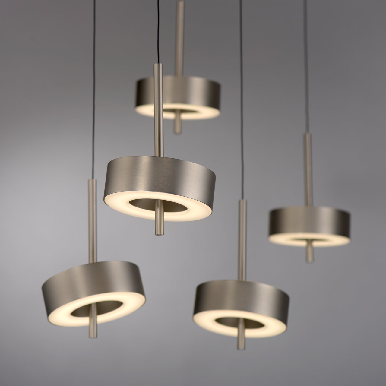 Moderne Pendelleuchte Q-ROTATE in gebürstetem Metall, von unten betrachtet, mit fünf leuchtenden Ringen.