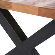 Nahaufnahme eines Esstisches mit einer robusten Holzplatte und einem schwarzen Metallgestell in X-Form, seitliche Perspektive.