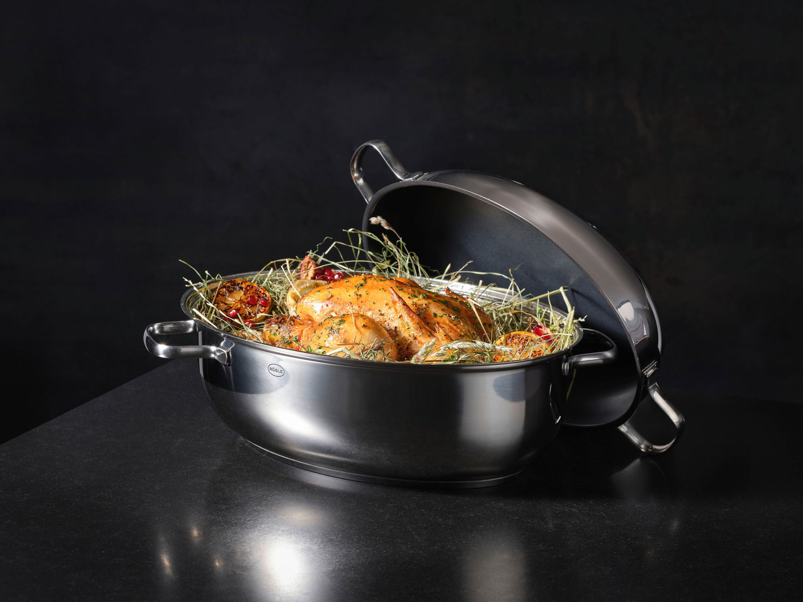 Eleganter ovaler Bräter mit Deckel, gefüllt mit einem gebratenen Hähnchen und Kräutern, seitliche Perspektive