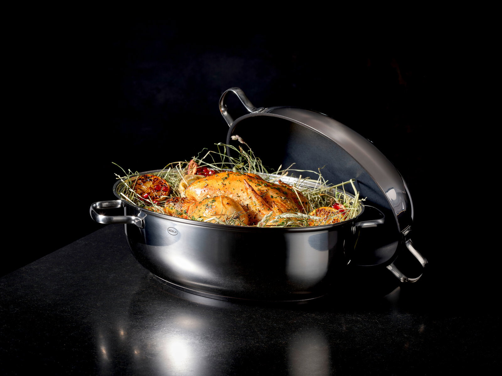 Rösle Bräter oval ELEGANCE Eleganter ovaler Bräter mit Deckel, gefüllt mit einem gebratenen Hähnchen und Kräutern, seitliche Perspektive