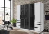 Moderner 5-türiger Drehtürenschrank in Schwarz und Weiß, frontal abgebildet in einem stilvoll eingerichteten Raum mit Backsteinwand und großen Fenstern.