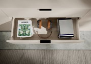 Een open lade van een tv-kast met boeken, koptelefoons en tijdschriften, gezien vanuit vogelperspectief.